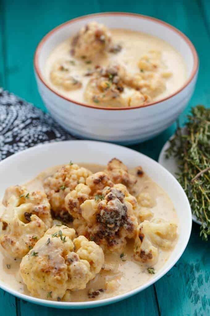 Roasted Cauliflower Soup on white plate and in white bowl on blue table