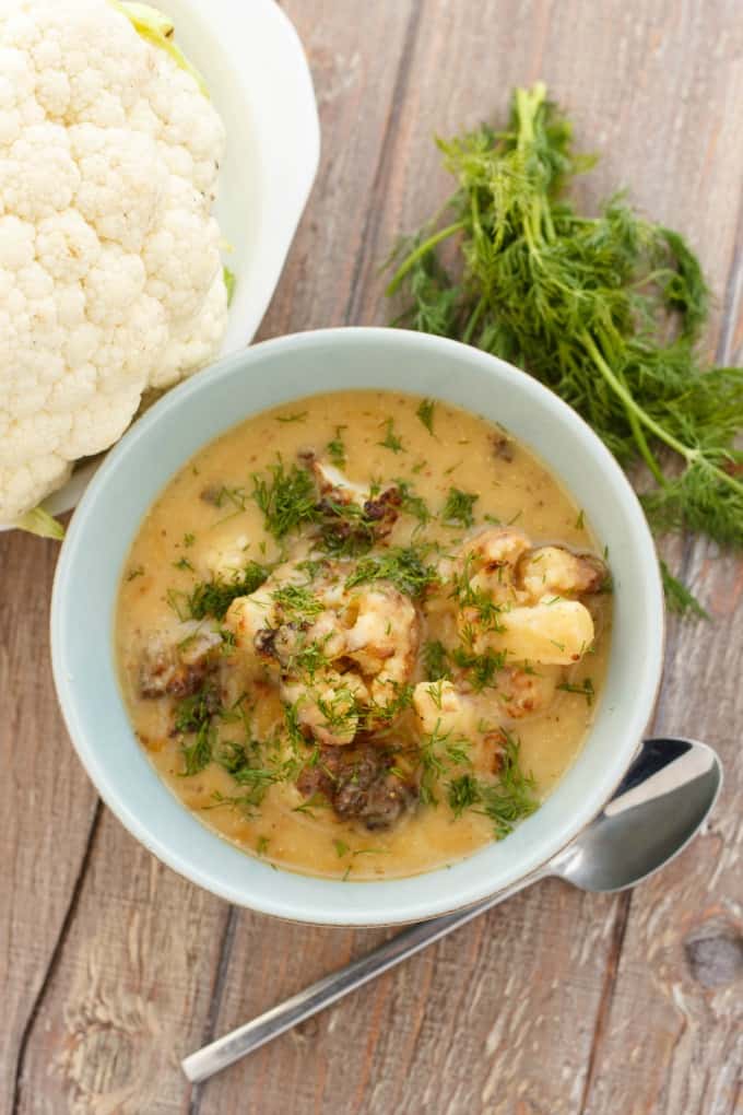 Vegan Roasted Cauliflower Soup on white bowl on brown table with spoon ,cauliflower and veggie #dill