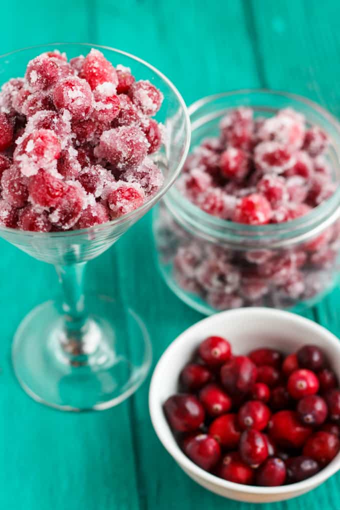 Candied Cranberries with Amaretto Liqueur in glass with glass ajr full of candied cranberries next to white bowl full of cranberries on blue table