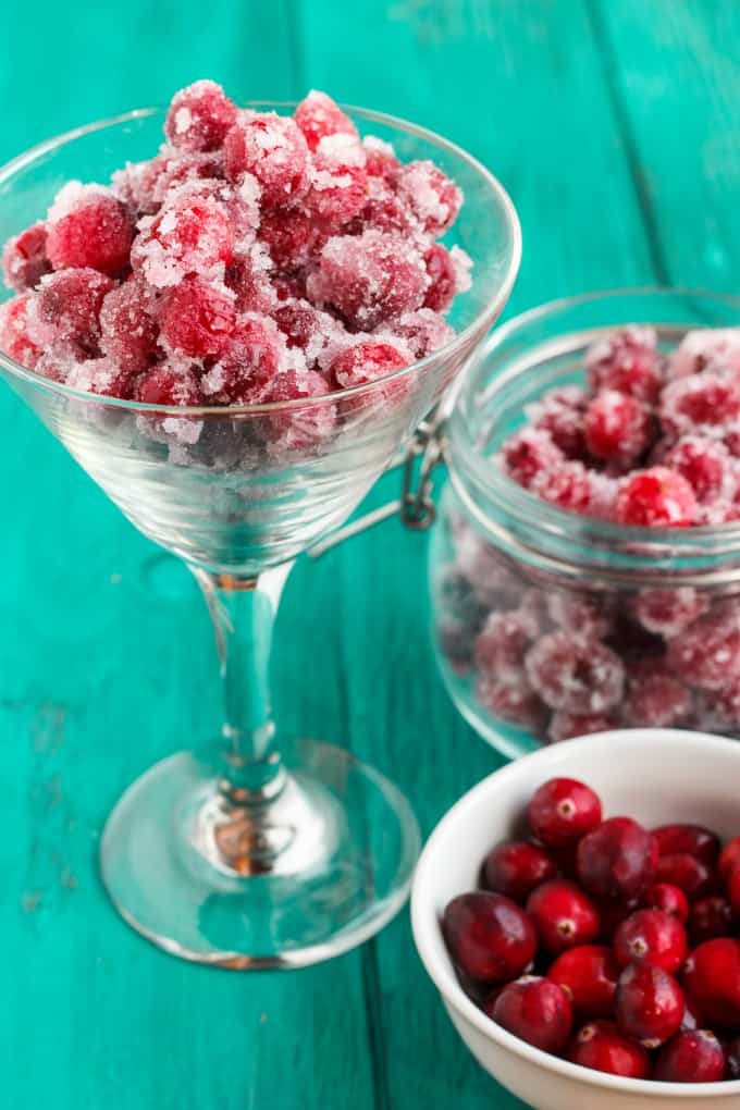 Candied Cranberries with Amaretto Liqueur in glass on blue table nexto to glass ajr  full of candied cranberries and white bowl full of cranberries
