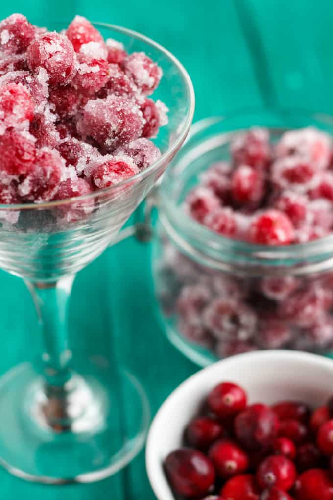 Candied Cranberries with Amaretto Liqueur in glass, jar and white bowl full of cranberries on blue table