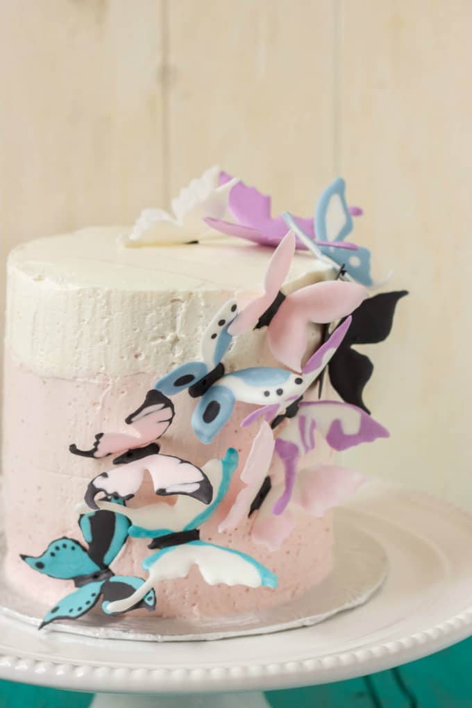 Pink Ombre Cake with Royal Icing Butterflies on white tray on blue table, white background