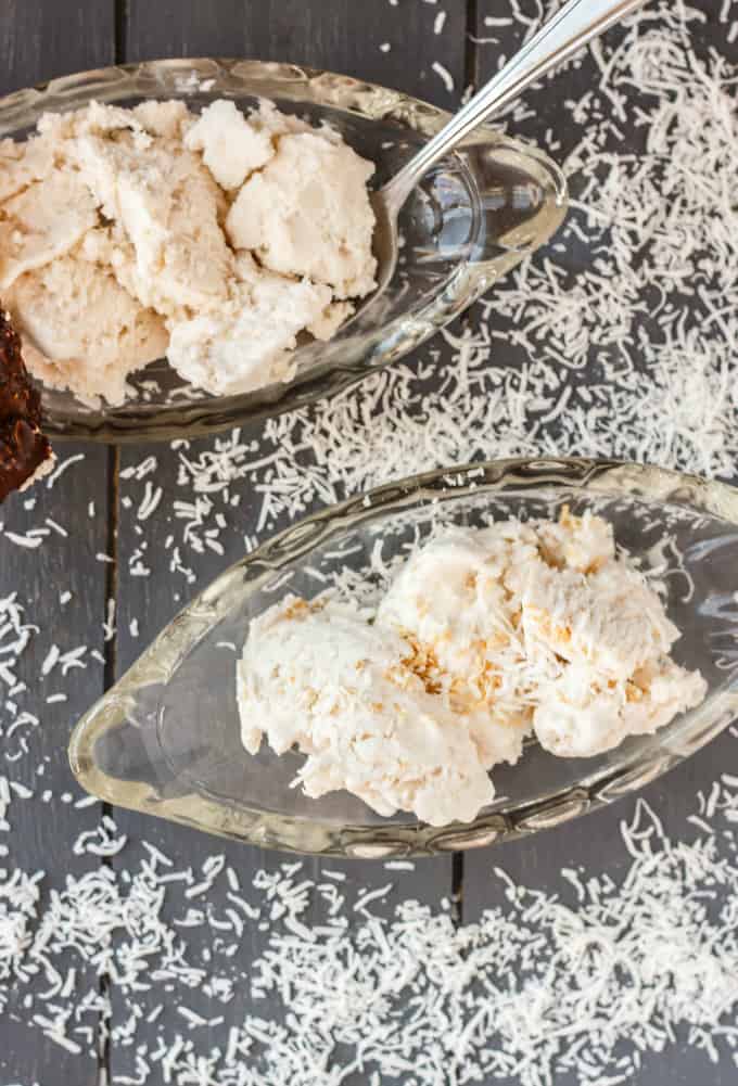 Vegan Toasted Coconut Ice Cream on glass trays with spoon on gray table with sliced coconut