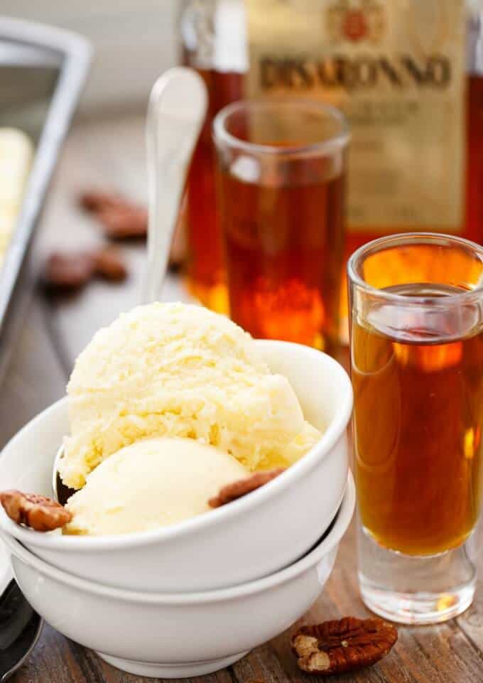 Amaretto Ice Cream in stack of white bowls on wooden table with spoon,nuts, glass shot full amaretto liquor and beotthe in the background#icecream