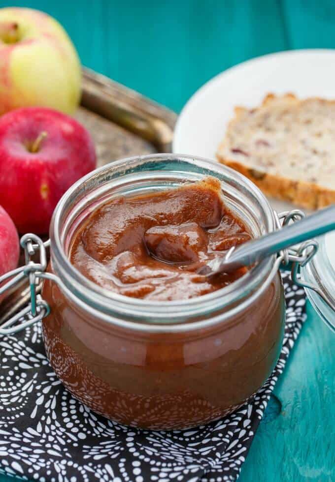 Apple Butter in the Slow Cooker in glass jar with knife nexto to apples and slice of bread on white plate on blue table