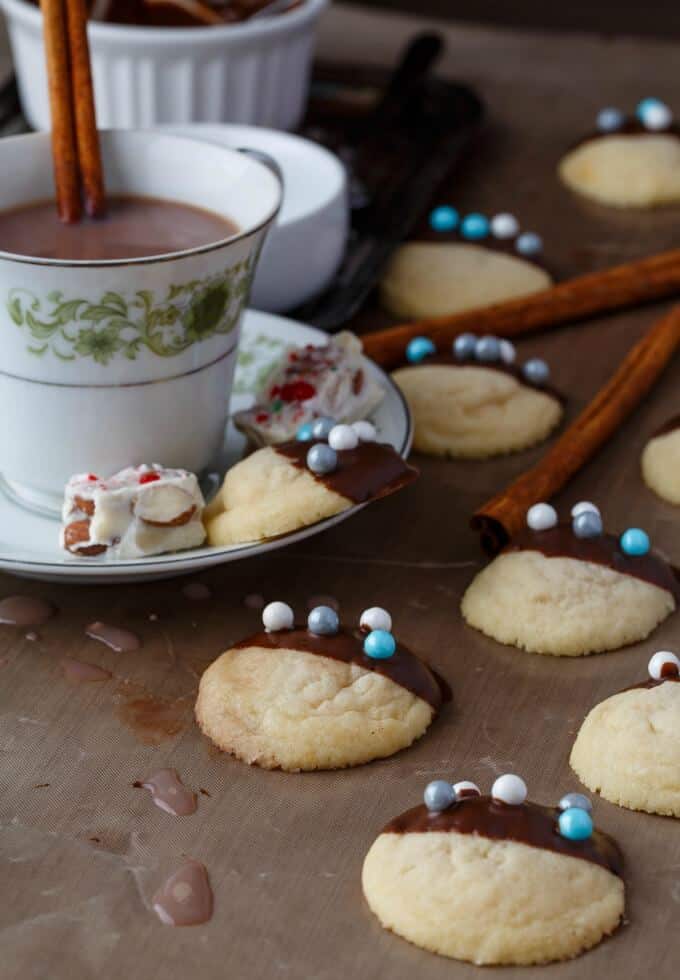 Chocolate dipped shortbread cookies on brown table next to cup with plate with liquid