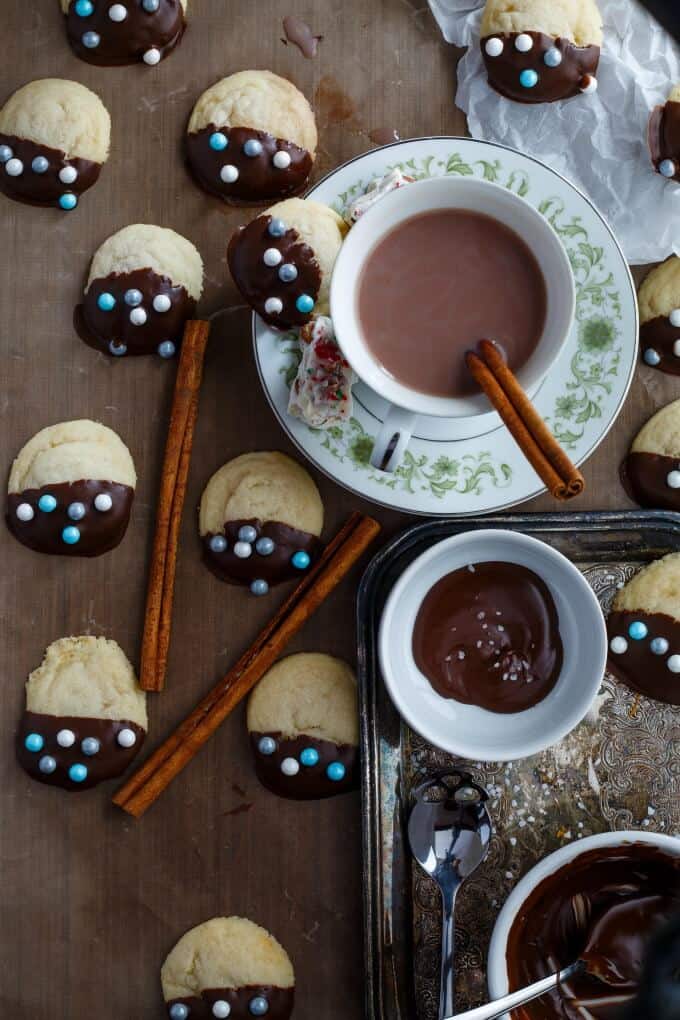 Chocolate dipped shortbread cookies on brown plate with cup with liquid on small plate, white bowl with chocolate dip