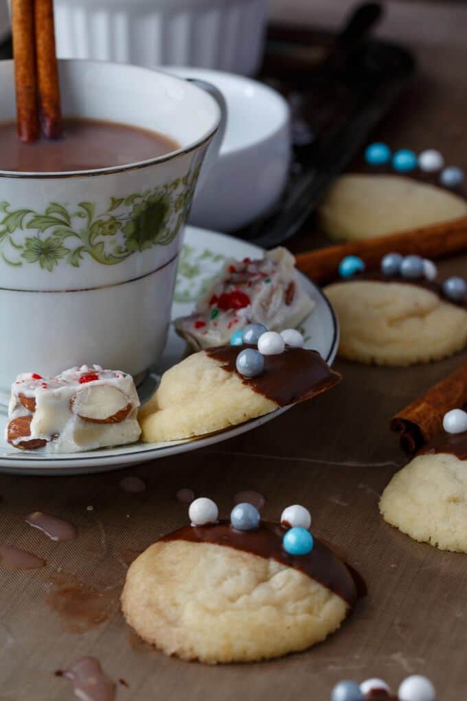 Chocolate dipped shortbread cookies on brown table next to cup with liquid with small plate