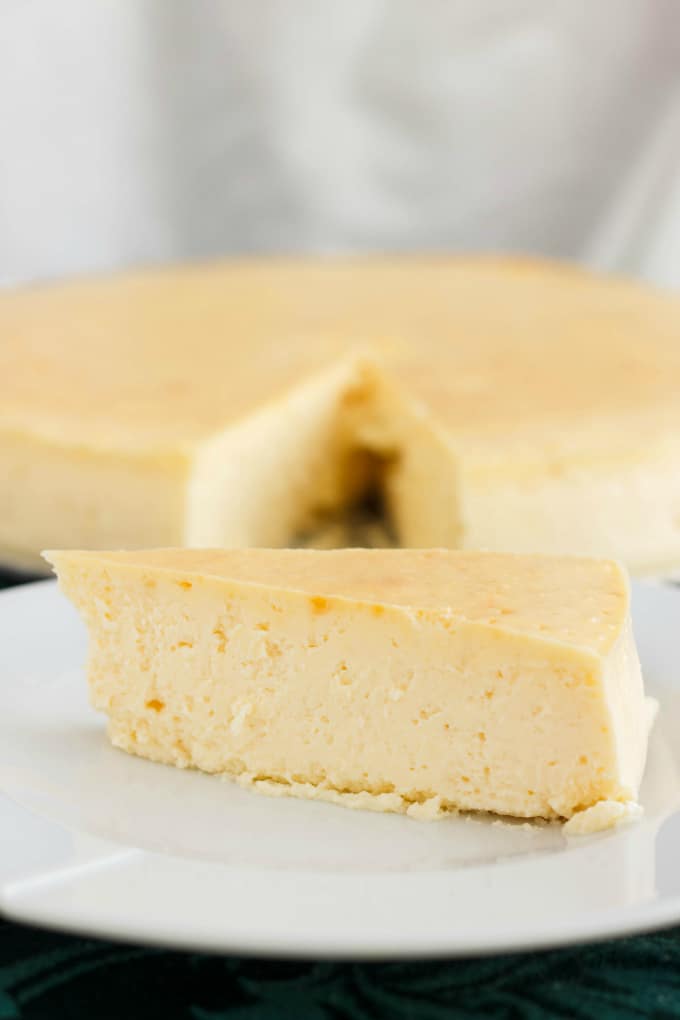 Crust-Less Lemon Cheesecake with Candied Cranberries slice on white plate, rest of cake on the background