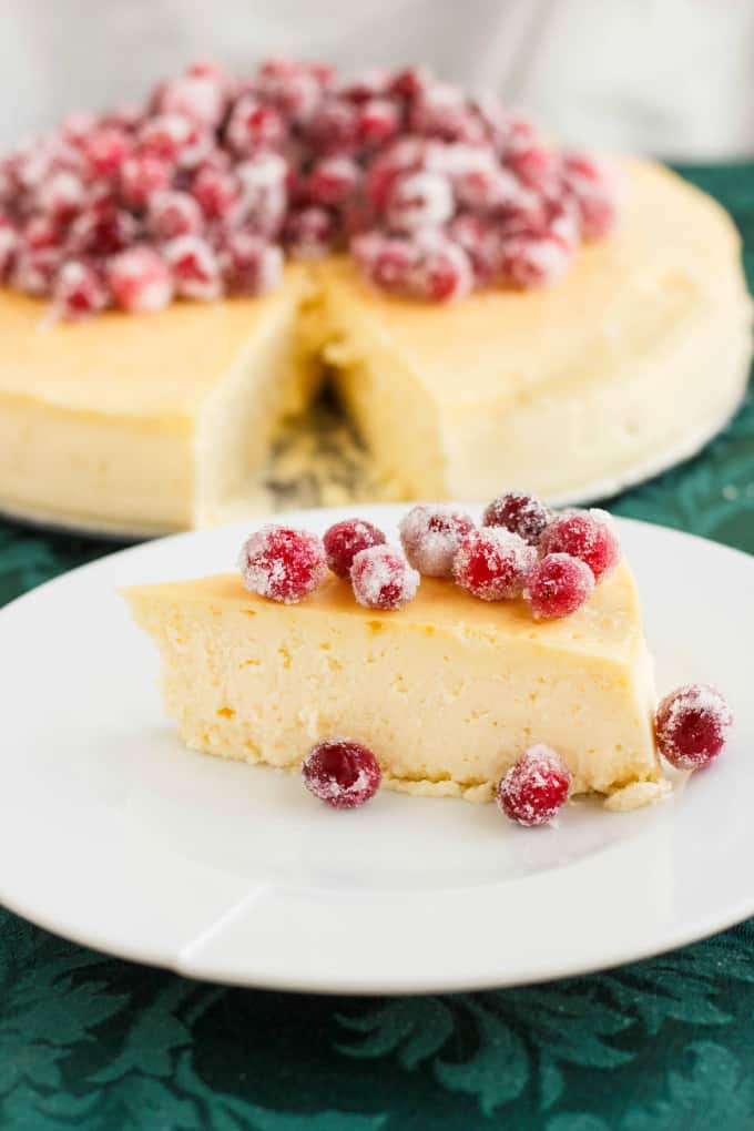 Crust-Less Lemon Cheesecake with Candied Cranberries slice on white plare, in the bacgkround rest of cheesecake
