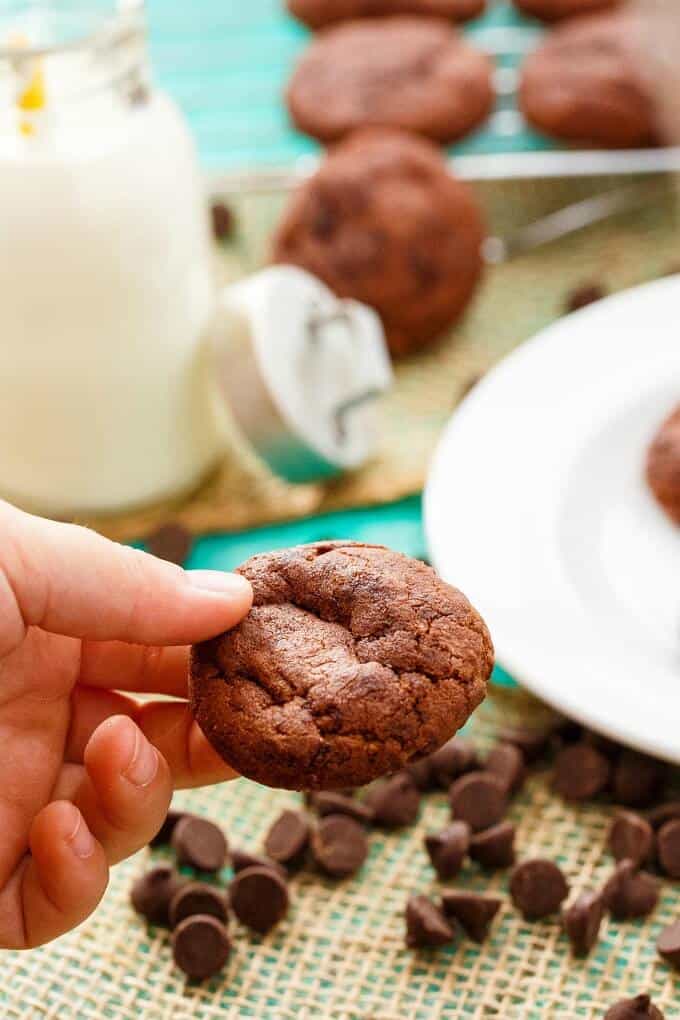 Double Chocolate Cookies with Hershey's Chipits held by hand, white plate and chocolate chips on table in the background