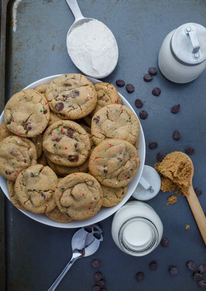 Gluten-Free Peppermint Cookies with Chocolate Chips on white plates with glass jars of milk, spoon with ingredients and scattered chocolate chips on black tray