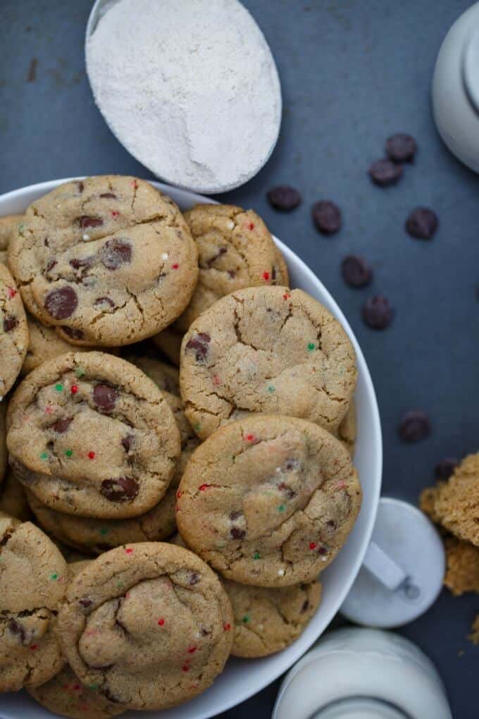 Gluten-Free Peppermint Cookies with Chocolate Chips on white plate on black table next to glass jar of milk, chocolate chips and flour in bowl