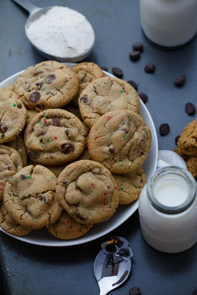 Gluten-Free Peppermint Cookies with Chocolate Chips on white plate on black table next to spoon, glass jar of milk and chocolate chips