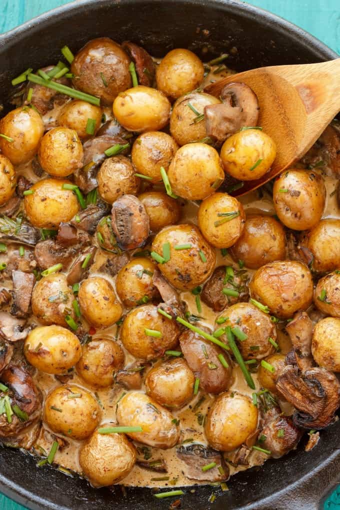 Roasted Baby Potatoes in a Homemade Mushroom Sauce  in black pan with wooden spatula on blue table#sidedish