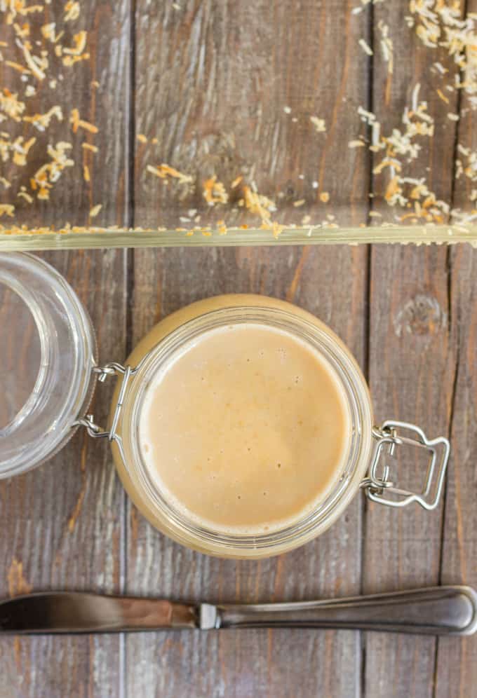 Toasted Coconut Butter in glass jar on wooden table next to knife