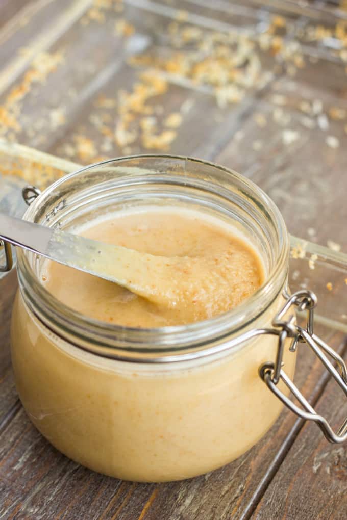 Toasted Coconut Butter in glass jar with knife in on wooden table with glass container