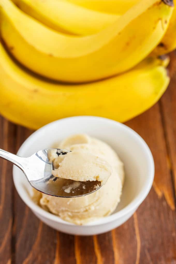 Banana Nice Cream (Banana Ice Cream) in white bowl picked by spoon on wooden table with bananas