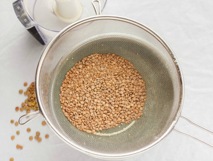 Lentil on kitchen strainer over container on white table and lentils