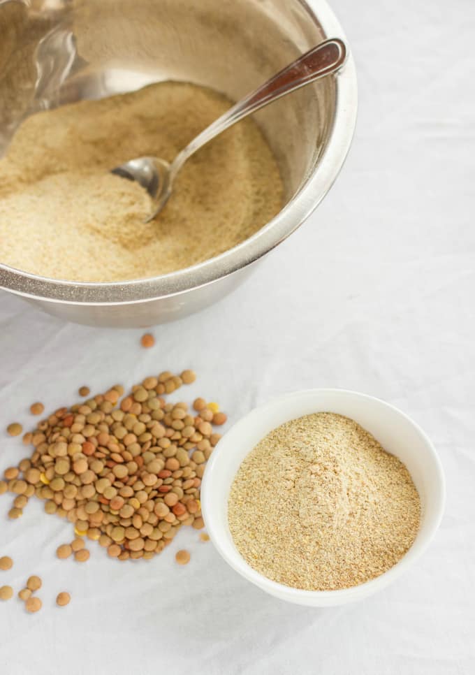 Homemade Lentil Flour in white bowl next to big bowl with spoon with lentil flour and lentils on the  white table