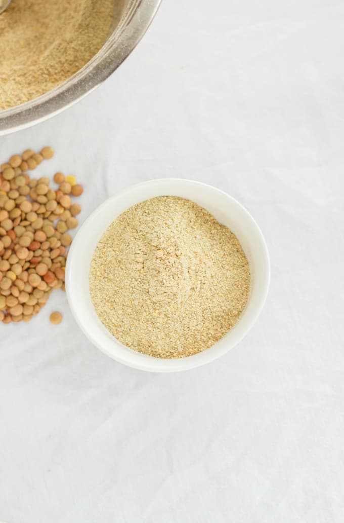 Homemade Lentil Flour in white bowl next to lentils and biger bowl on white table