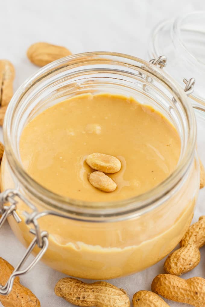 Homemade Peanut Butter in glass jar with lid and peanuts on white table