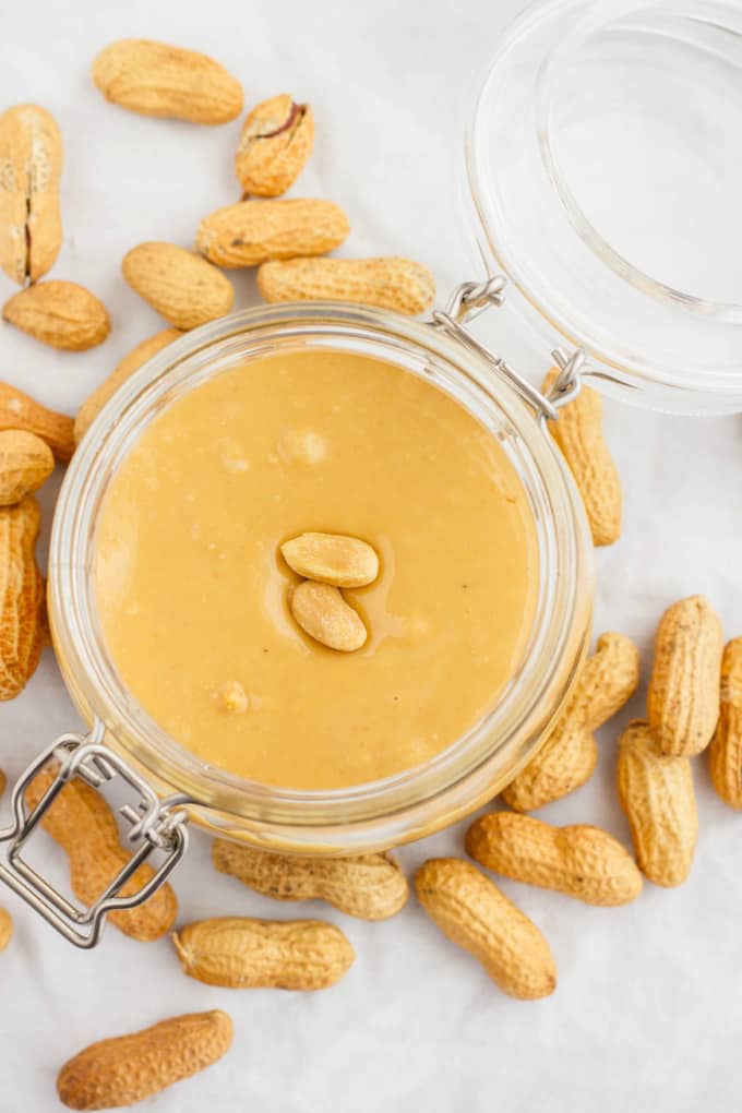 Homemade Peanut Butter in glass jar with lid on table with peanuts