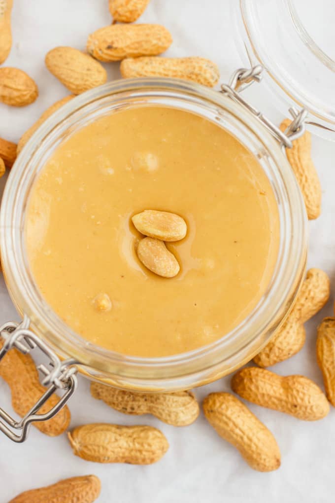 Homemade Peanut Butter in glass jar with peanuts on white table