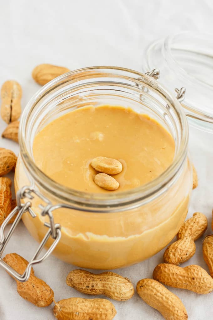 Homemade Peanut Butter in glass jar with li with peanuts on table