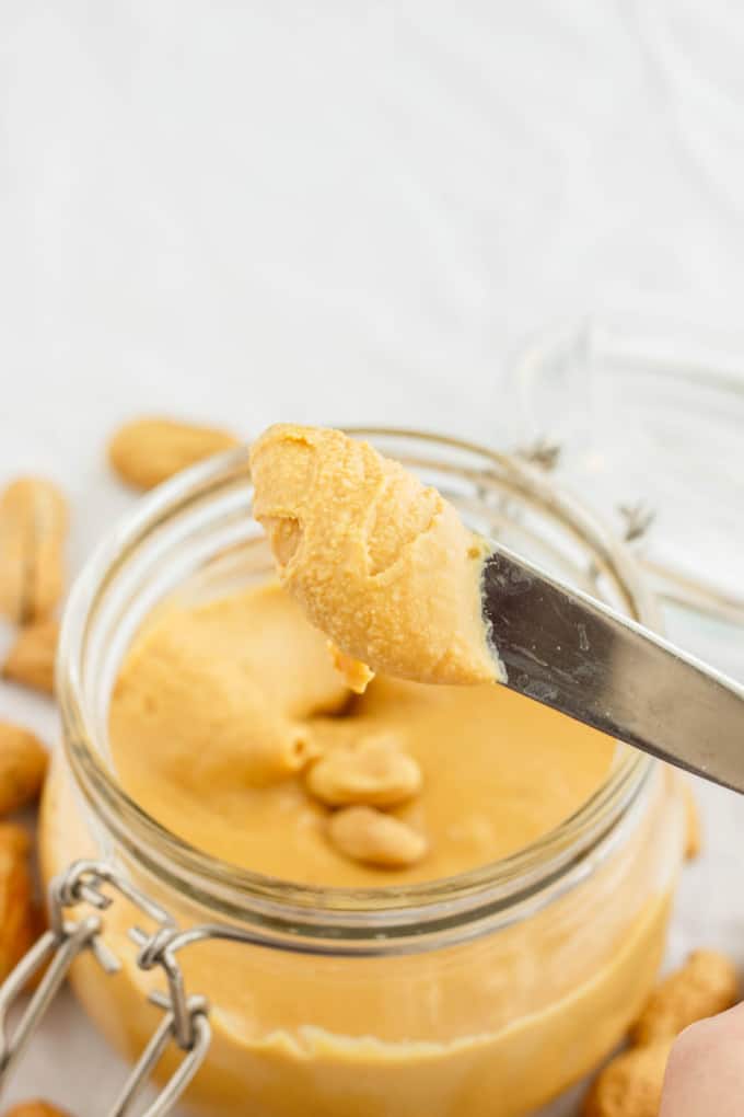 Homemade Peanut Butter in glass jar picked by knife with peanuts