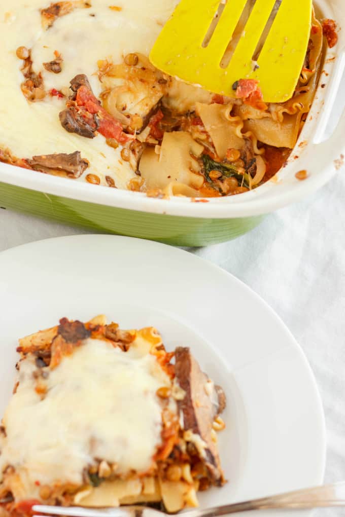 Lentil Lasagna in a Roasted Portobello Cream Sauce on white plate and in baking pot with yellow spatula on white table