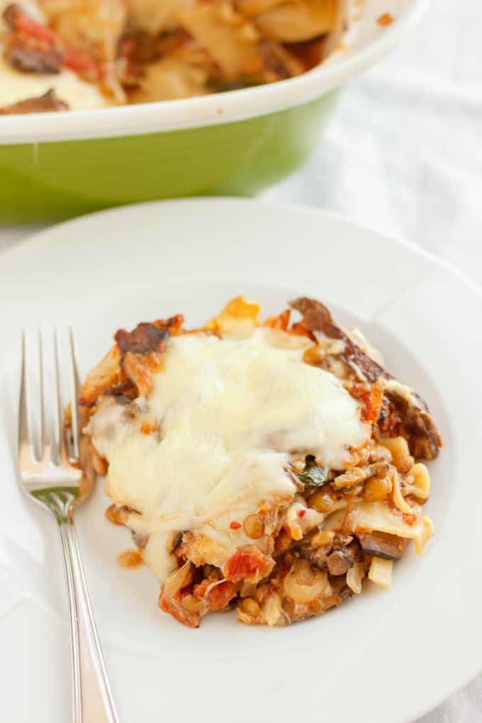 Lentil Lasagna in a Roasted Portobello Cream Sauce on white plate with fork, green baking pot in the background