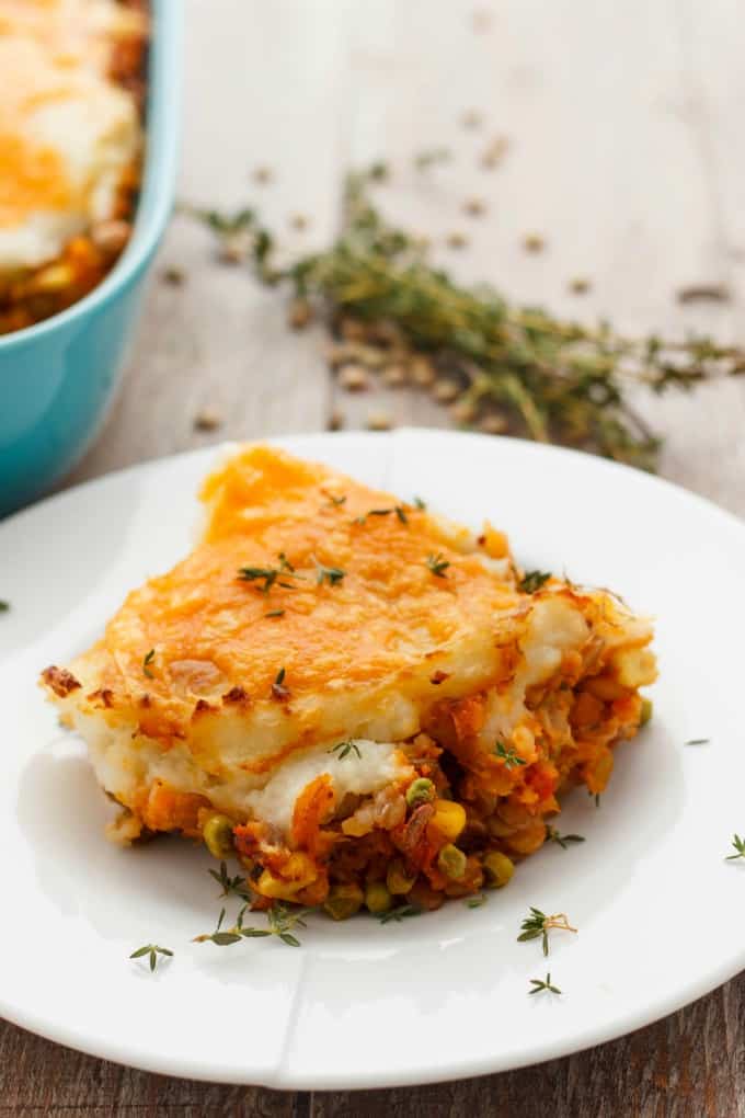 Vegetarian Shepherd's Pie  slice on white plate on wooden table, veggie nad baking pot  in the background(Vegan Shepherd's Pie Included.)