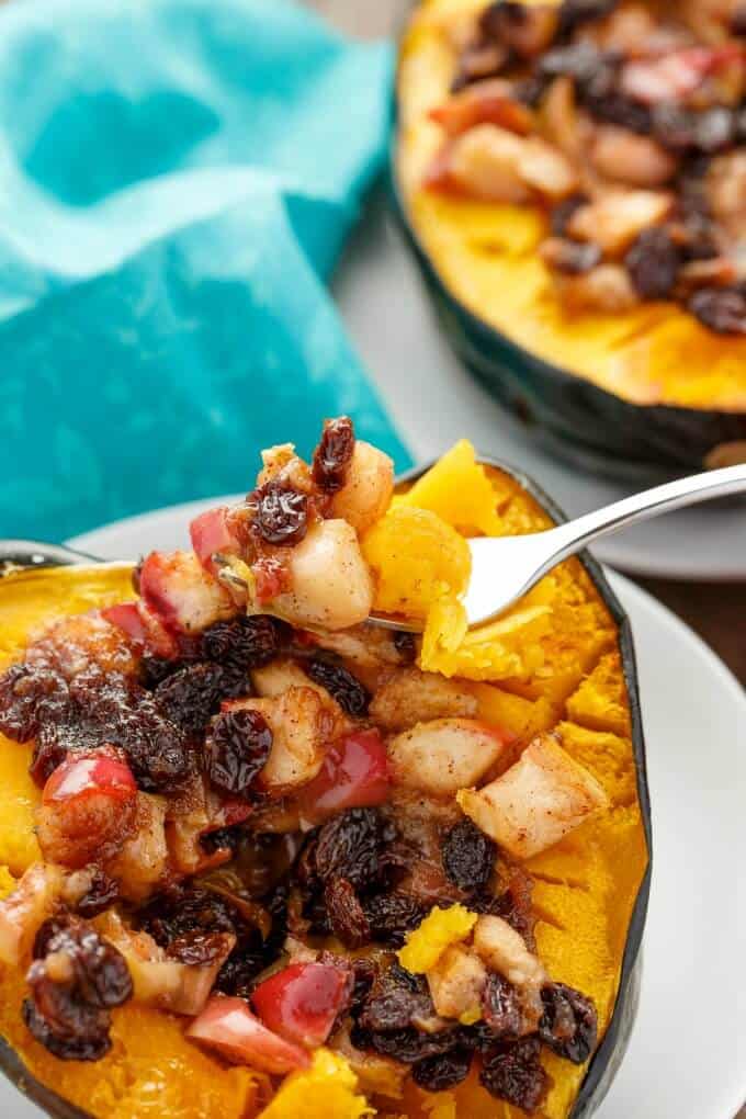 Acorn squash stuffed with apple and raisins picked by fork on white plate