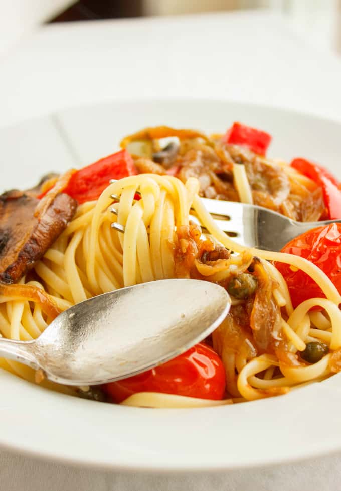 Artichoke Hearts, Caramelized Onions and Roasted Portobello Mushroom Pasta on white plate with spoon and fork, close view