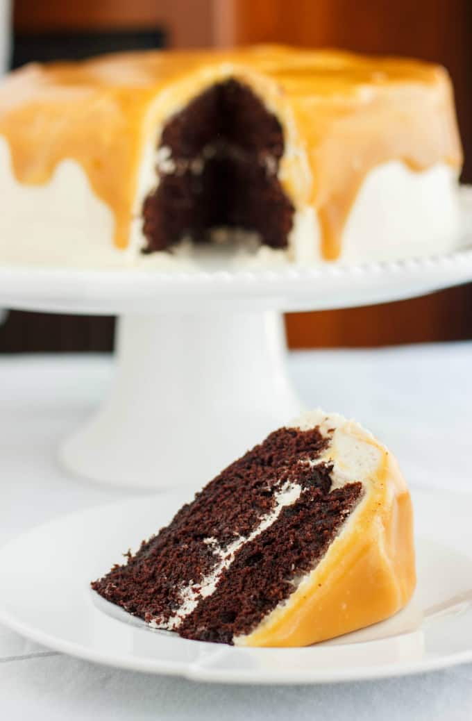 Caramel and Coffee Layer Cake slice with Coffee Buttercream on white plate, cake on white stray in the background