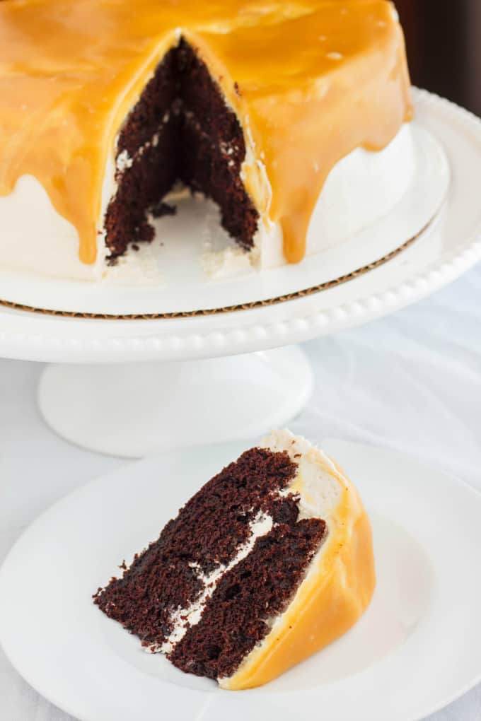 Caramel and Coffee Layer Cake slice with Coffee Buttercream on white plate, whole cake on white tray on white table