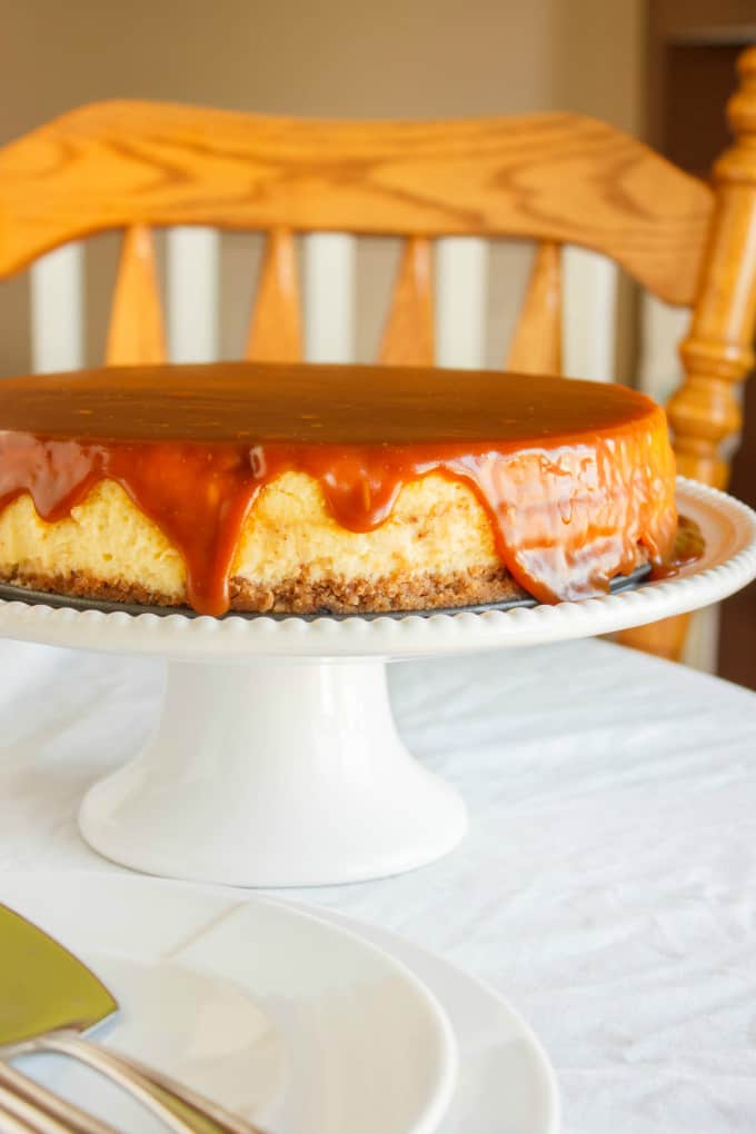 Salted Caramel Cheesecake on white tray on white table, wooden chair in the background