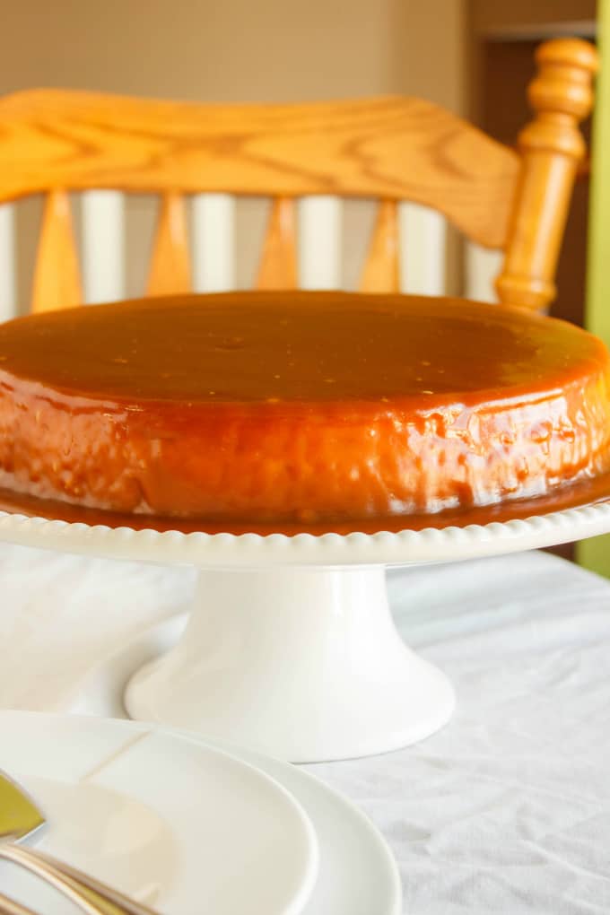 Salted Caramel Cheesecake on white tray on white table, wooden chair in the background