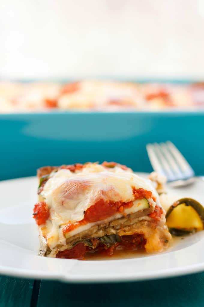 Eggplant and Zucchini Lasagna on white plate with fork on blue table, in the background blue baking pot with same dish (No Pasta!)