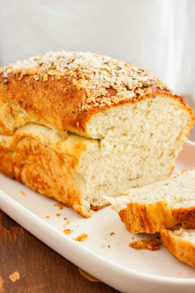 Herb and Cheese Bread loaf and two slices on white tray on wooden table