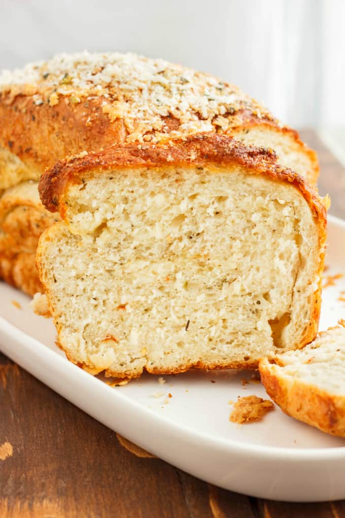 Herb and Cheese Bread loaf and two slices on white tray on wooden table