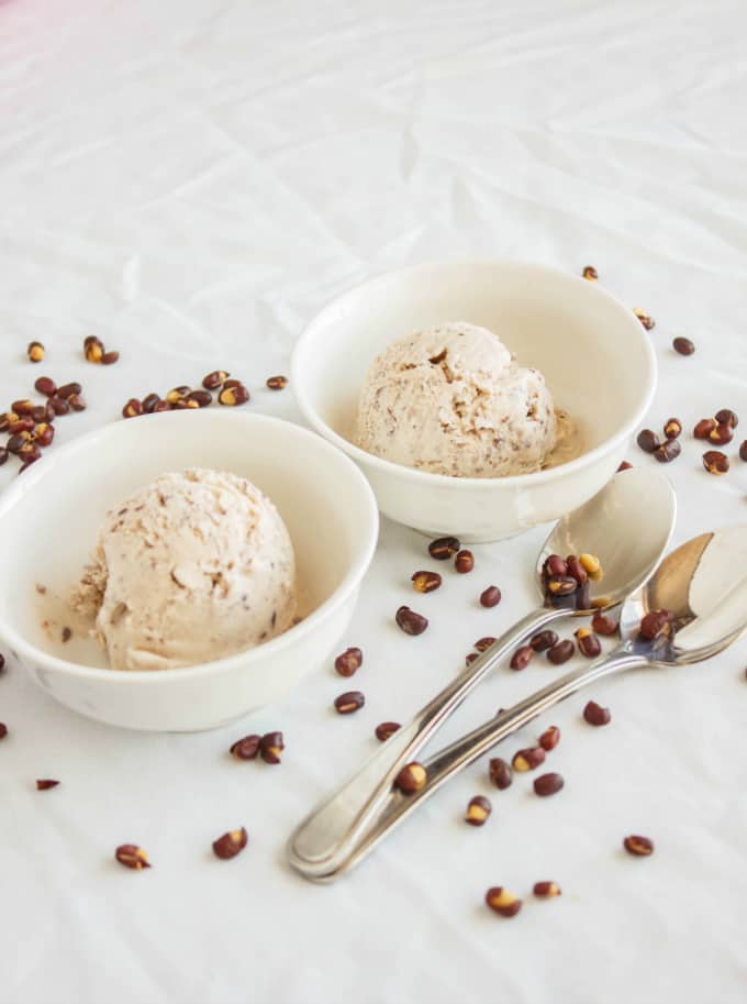 Red Bean Ice Cream in white bowls with two spoons and spilled red beans around