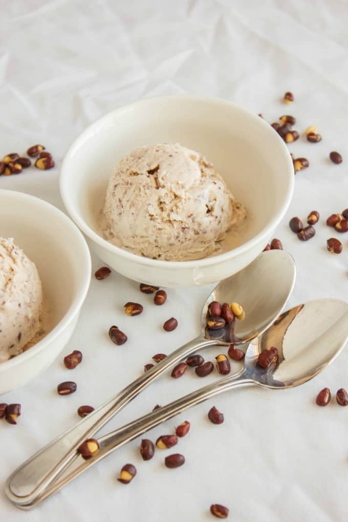 Red Bean Ice Cream in white bowl with two spoons with spilled red beans around