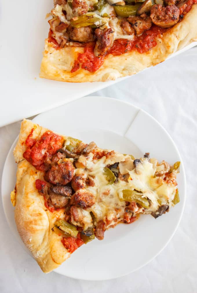 Sausage Pizza with Onions, Green Peppers, and Bacon on white tray, slice of pizza on white plate