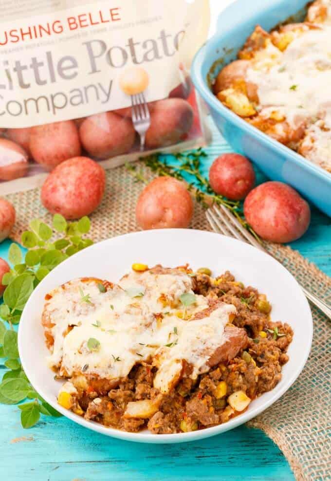 Smashed Potato Shepherd's Pie on white plate on blue table with fork, potato sack, veggies,potatoes and baking pot with same dish(Cottage Pie)