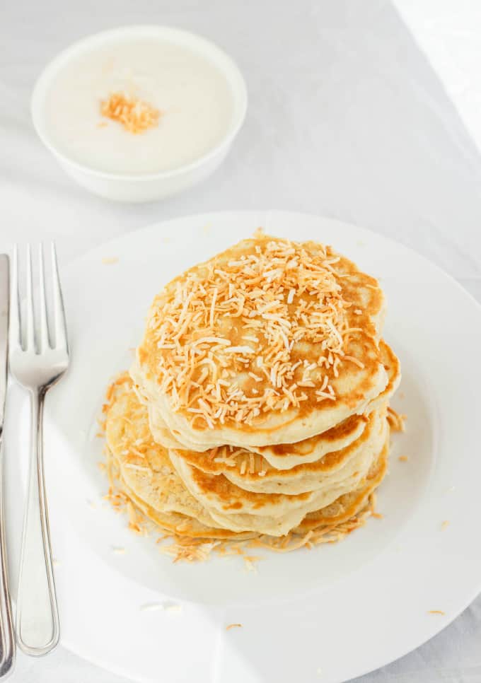 Toasted Coconut Pancakes on white plate with fork on white table with bowl