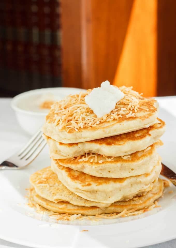 Toasted Coconut Pancakes on white plate with fork on white table