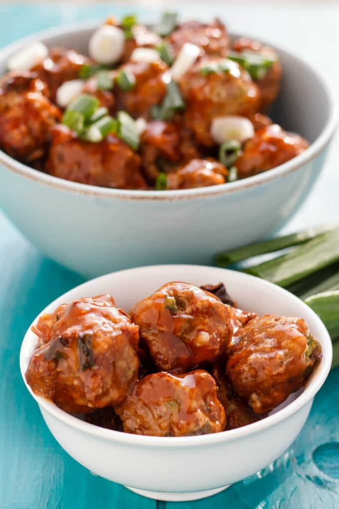 General Tso's Meatballs in white bowl with veggies on blue table#meatballs