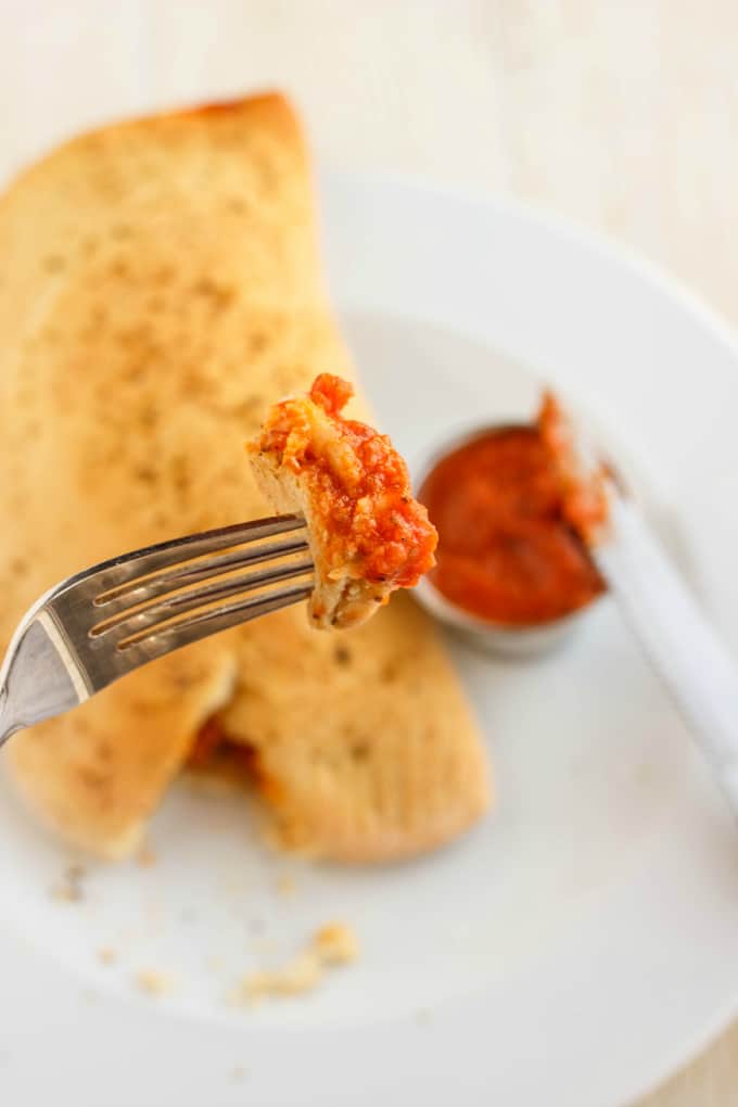 Homemade Calzones on white tray with dip and knife, piece of dish picked on fork